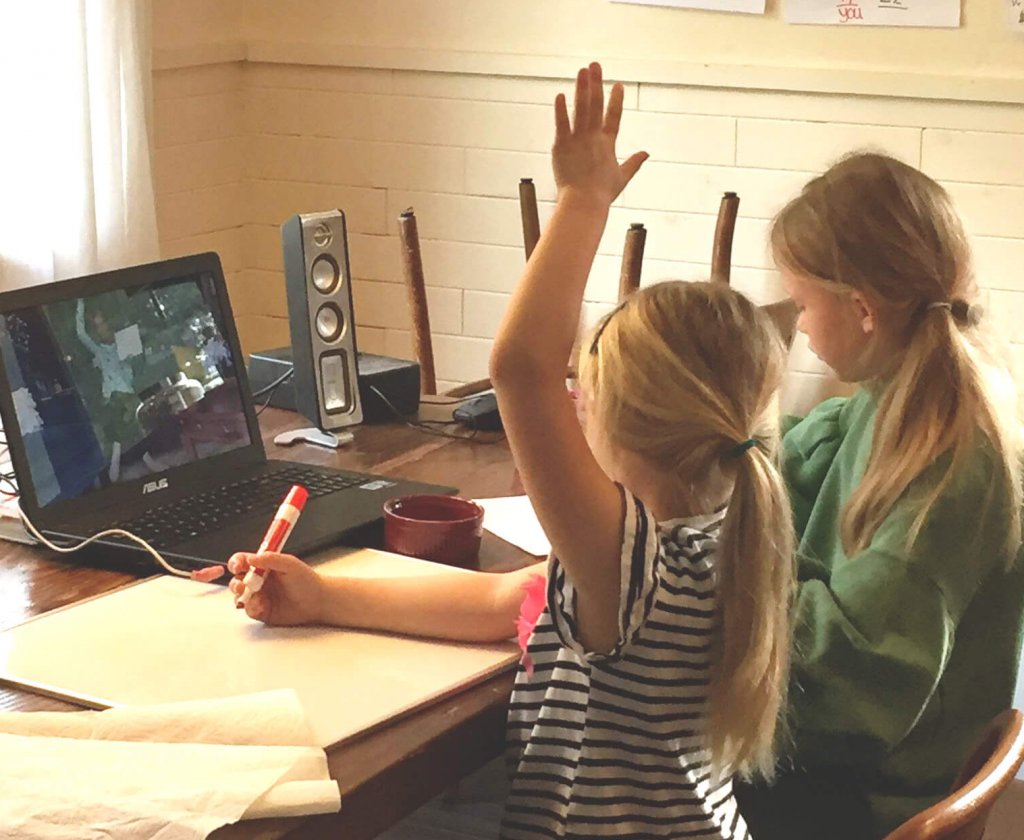 a kindergartner raises her hand while looking at a computer in her house