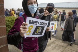 Student holding sign reading David > Cancer