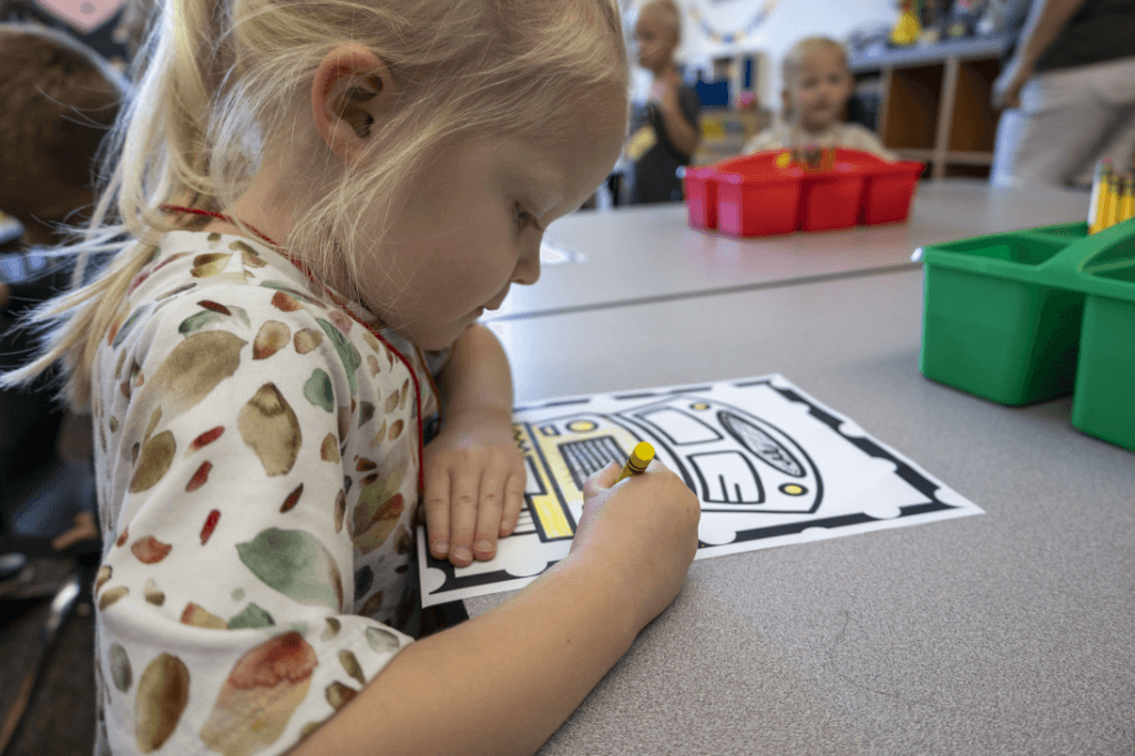 young girl coloring a school bus picture
