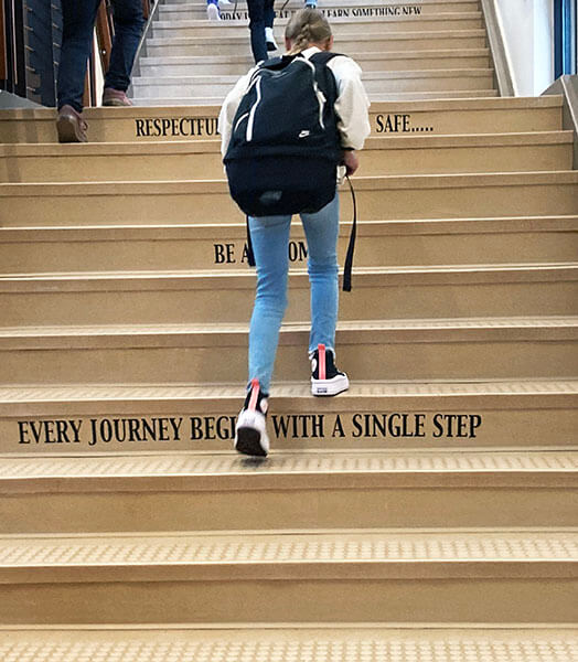 Student climbs the stairs to school. Imprinted on one of the stairs is "Every journey begins with a single step."