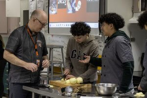 A teacher works with two students during a culinary arts class