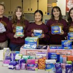 A teacher and four high school students pose with menstrual products collected as part of a donation drive